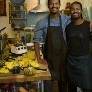 Two men smiling with smoothie making things on a table