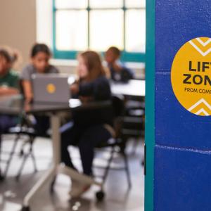 Children in a classroon using laptops. "Lift Zone" sticker on the outside wall of the room.