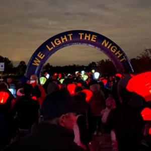 "We light the night" banner, red lanterns held by a group of participants at a nighttime event.