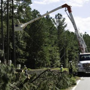 Line workers, one in a bucket-lift, repairing down power lines.