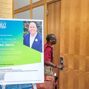 A person entering a meeting room. A sign for "The financial literacy coach" outside the door. 