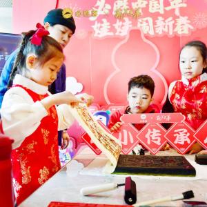 children watch as one lifts a piece of paper off an ink block. Signs in Chinese behind them and to the sides.