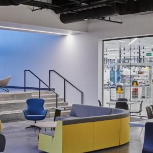 A lobby with blue and yellow seats, which also has a large window looking into a lab