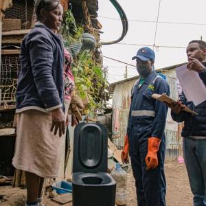 Two people talking to another, the loope toilet between them. 