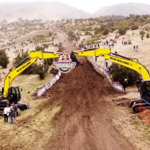Two large excavators with booms extended over a long dirt path.