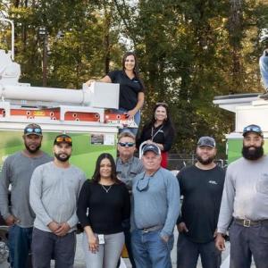 A large group of employees posed in front of two large trucks with extension buckets.