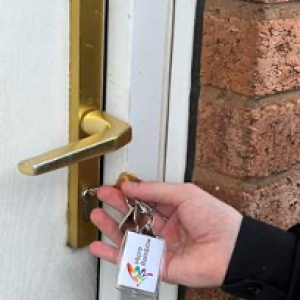 hand holding key with micro rainbow logo in front of an exterior door