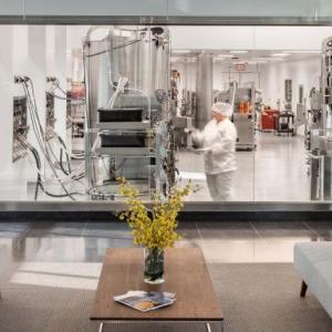 An office building with clear window-walls surrounding a lab with large equipment.
