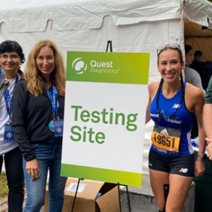 a group of five people, one in running apparel, by a sign for Quest "Testing Site" and a white tent behind them