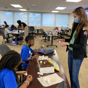 an adult works with two students at a desk to make marshmallow molecules
