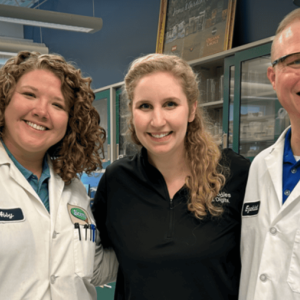 Three people posed together, two in lab protective wear.