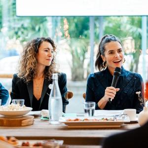People seated at a dining table. One speaking with a microphone.