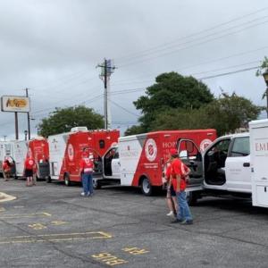 A row of parked box trucks in a parking lot, a person standing by each driver side door.