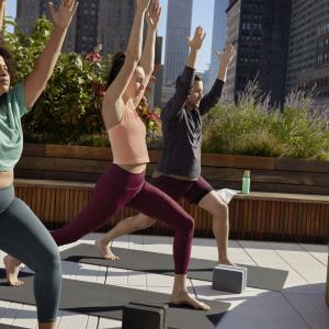 three people doing yoga pose on a rooftop, tall buildings around them