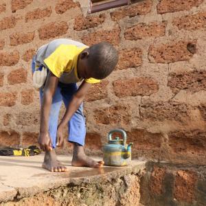 Konkourona child washes their feet with water from a small kettle