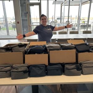 volunteer standing behind a table full of square gray zippered bags
