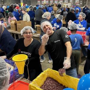 A large room full of volunteers in hair nets, packing food, two smiling to the camera