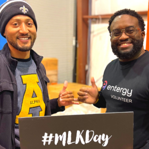Two people holding a sign "MLKDay" and giving thumbs-up.