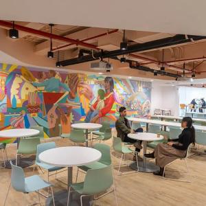 Two people at a circular table in a cafeteria type setting, a colorful mural on one wall.