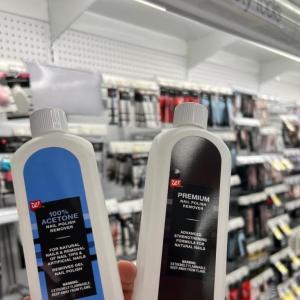 Two bottles of nail polish remover in slightly different packaging, held up in front of an aisle of beauty products.