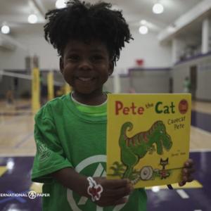 in a gym, a child with a big smile shows a book