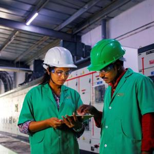 Two people in uniforms and hard hats, one pointing at a tablet being held by the other.