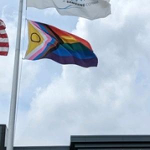 A flag pole with HARMAN and LGBTQ+ flag flying