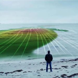 A person on a beach overlooking a body of water. A digital topography overlayed.