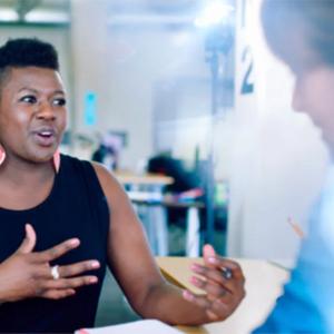 two people taking, seated at a desk across from each other