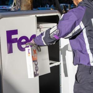A person in FedEx uniform opening a tall cart with FedEx Express logo on it and pulling out a package.