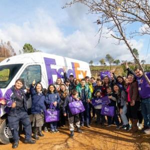 A group of volunteers and children posed in front of a fedex truck.