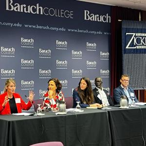 A panel of five people at the front of a room, one speaking.