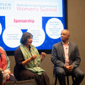 A four person panel, one speaking. A digital screen "Paradigm for Parity" showing.