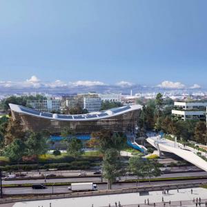 Aerial view of a large stadium, a bridge going over a busy road to it.