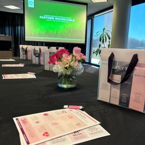 A table set with gift bags, papers and a pen. A small bouquet of flowers central. A pull-down screen in the background.