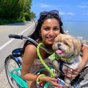 A person biking outside with a small dog in a front basket.