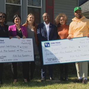 People standing in front of house holding oversized checks
