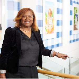 Kelie Charles is pictured in a black suit smiling at the camera with images of Bath & Body Works products are displayed on a wall behind her.