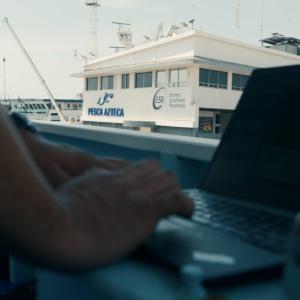 A person working at a laptop, a fishing boat outside their window.