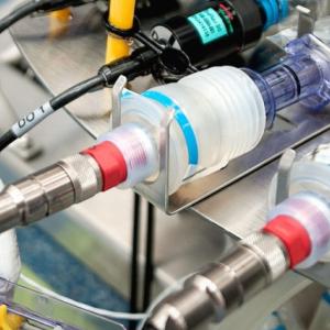 a gloved hand holding tubing into a machine