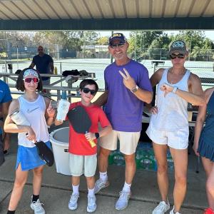 A group posed under a roof, some with pickleball equipment