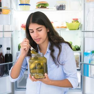 Person leaving fridge open while eating pickles
