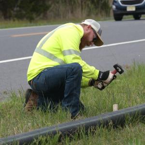 Volunteer working with a drain pipe on the side of a road.