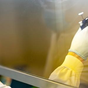 a scientist in protective gear, working behind a glass divider, using a pipette