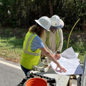 Two people in hard hats looking over a map on a table in front of a truck outside
