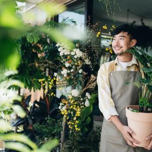 A smiling person holding a potted plant. Other plants hung around them.