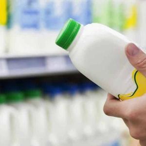 A person in a grocery store looking at a plastic container full of white liquid.
