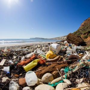 Plastic garbage on a beach, waves in the distance.