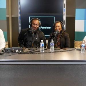 Four people at a large table, each wearing headphones and have a microphone in front of them.