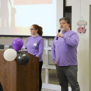 Two people in matching purple shirts behind a podium.